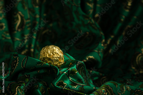 Tasty Chocolate Praline Wrapped with Golden Foil on Gorgeous Green Backdrop