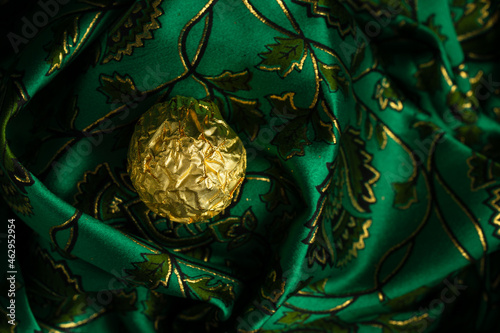 Tasty Chocolate Praline Wrapped with Golden Foil on Gorgeous Green Backdrop