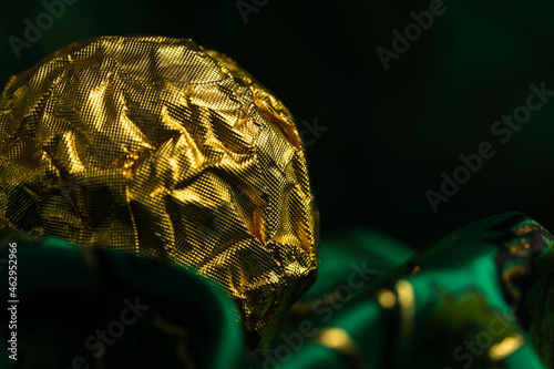 Tasty Chocolate Praline Wrapped with Golden Foil on Gorgeous Green Backdrop