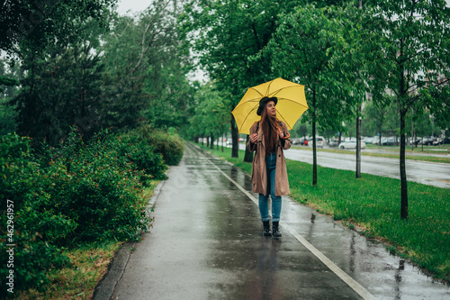 Woman holding a yellow umbrella and enjoying a walk in the park during rain