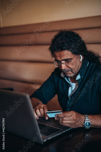 Senior hispanic cuban men using laptop and a credit card while online shopping