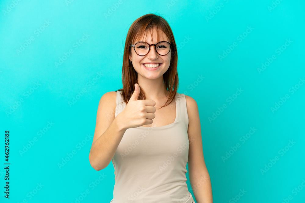 Redhead girl isolated on blue background giving a thumbs up gesture Redhead girl isolated on blue background giving a thumbs up gesture