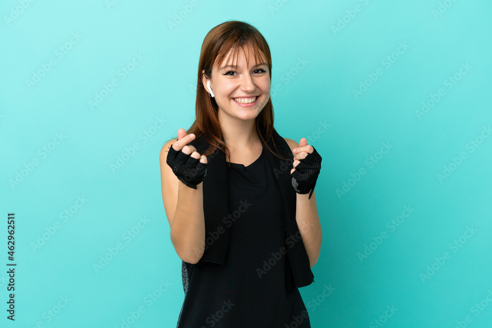 Redhead sport girl isolated on blue background making money gesture Redhead sport girl isolated on blue background making money gesture