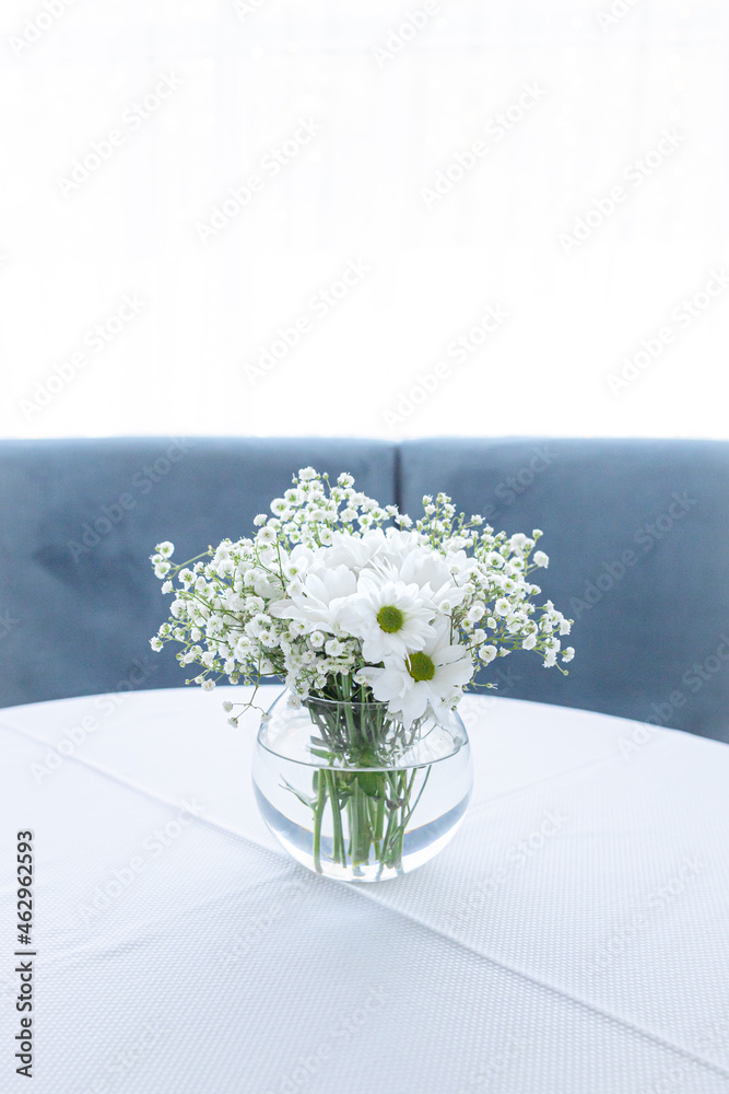 Fototapeta premium Round glass vase. White flowers. Light room. White color in the interior. Wedding decorations. Bright kitchen. Cozy place. Romantic bouquet. Cozy white kitchen. A room flooded with light.