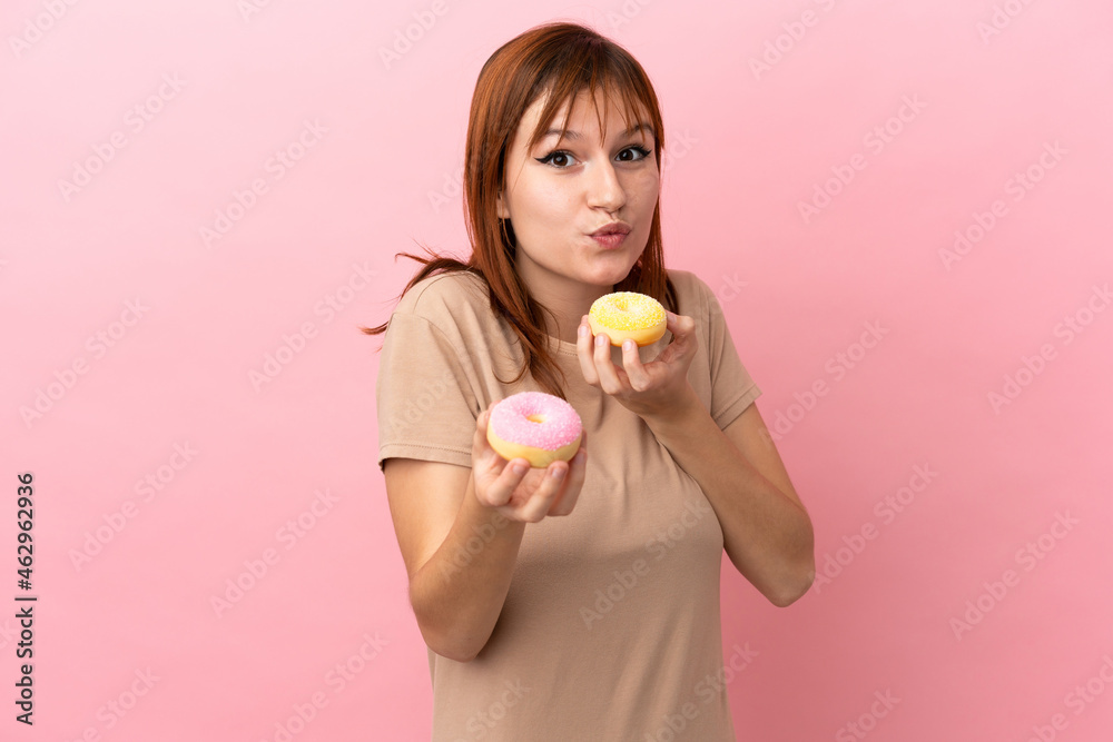 Redhead girl isolated on pink background holding a donut Redhead girl isolated on pink background holding a donut