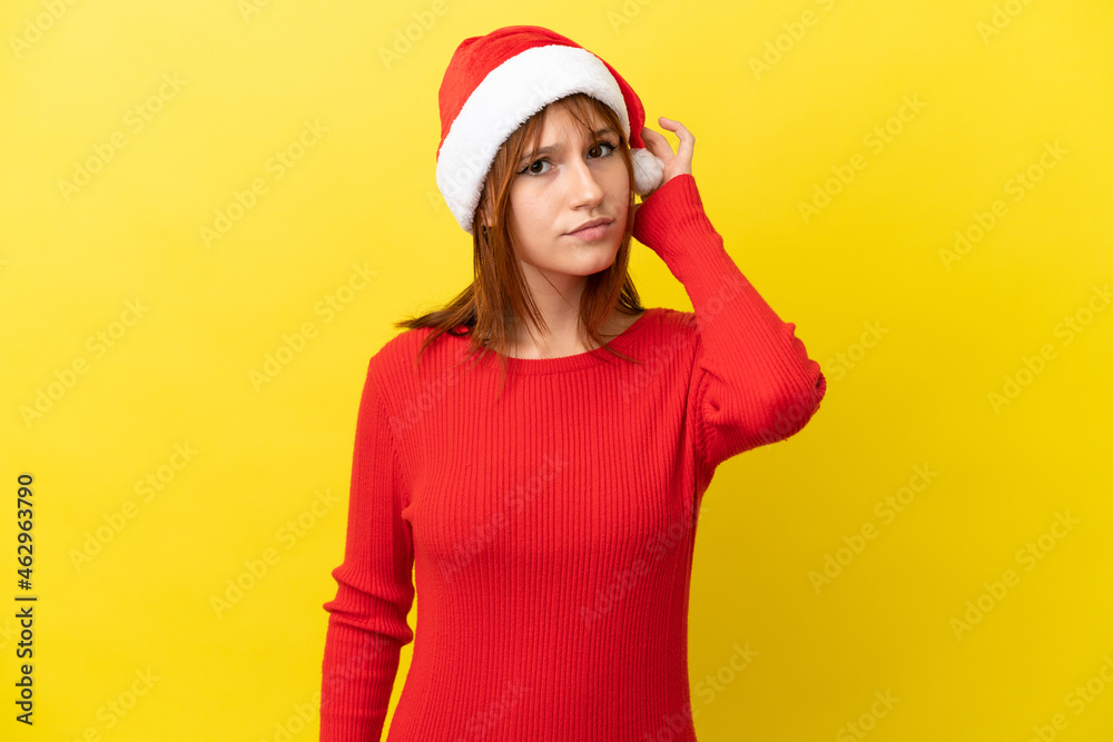 Redhead girl with christmas hat isolated on yellow background having doubts Redhead girl with christmas hat isolated on yellow background having doubts