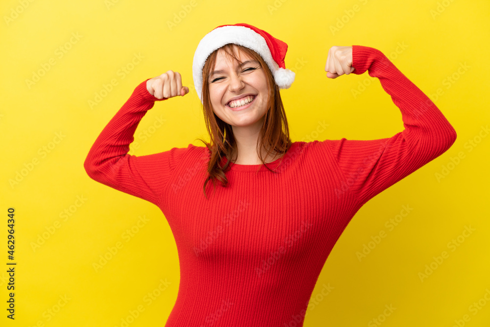 Fototapeta premium Redhead girl with christmas hat isolated on yellow background doing strong gesture