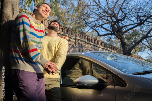 Latin gay couple holding hands and laughing in a funny moment while standing next to a car.