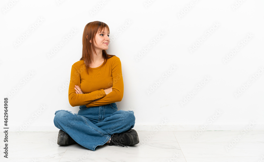Redhead girl sitting on the floor isolated on white background in lateral position