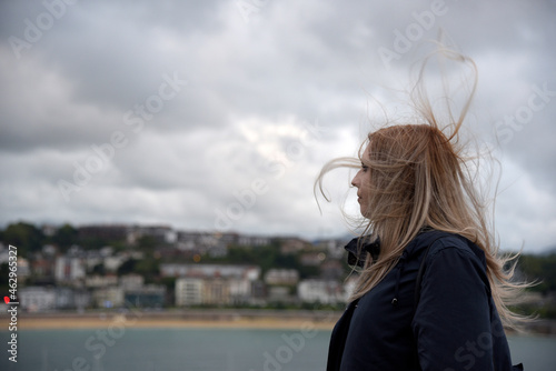 Una mujer rubia con el pelo al viento y ropa negra mirando hacia el mar en San Sebastian. 