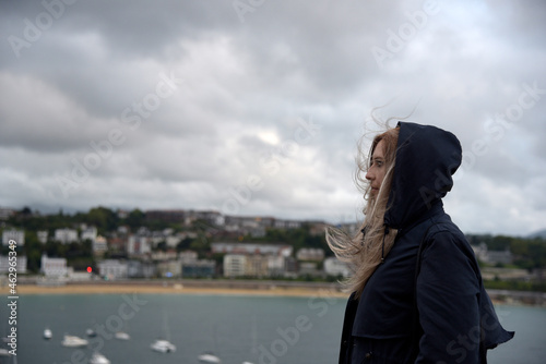 una mujer con el pelo rubio y ropa negra mirando hacia el mar en un dia de otoño con el cielo cubierto