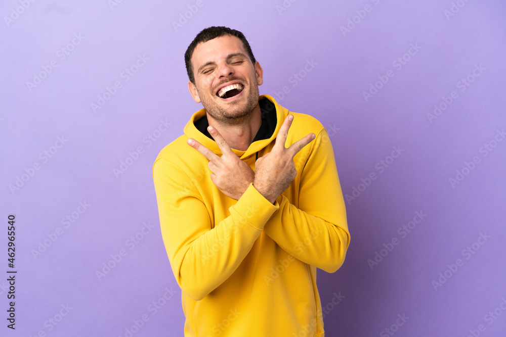 Brazilian man over isolated purple background smiling and showing victory sign