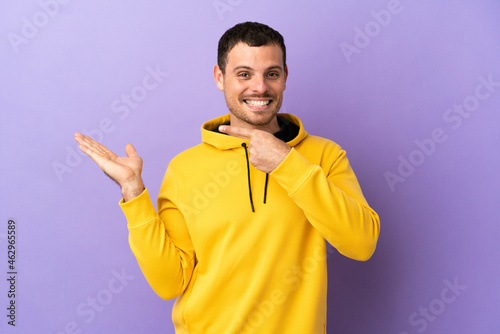 Brazilian man over isolated purple background holding copyspace imaginary on the palm to insert an ad
