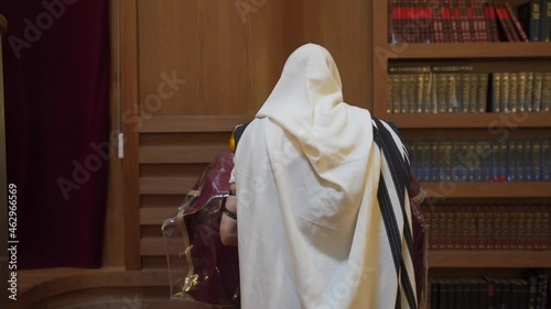 A Jew prays in the synagogue. A man stands near the presidium and reads a book. Rear view photo
