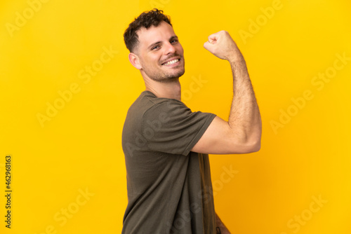 Young caucasian handsome man isolated on yellow background doing strong gesture