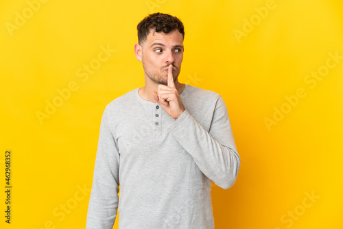 Young caucasian handsome man isolated on yellow background showing a sign of silence gesture putting finger in mouth
