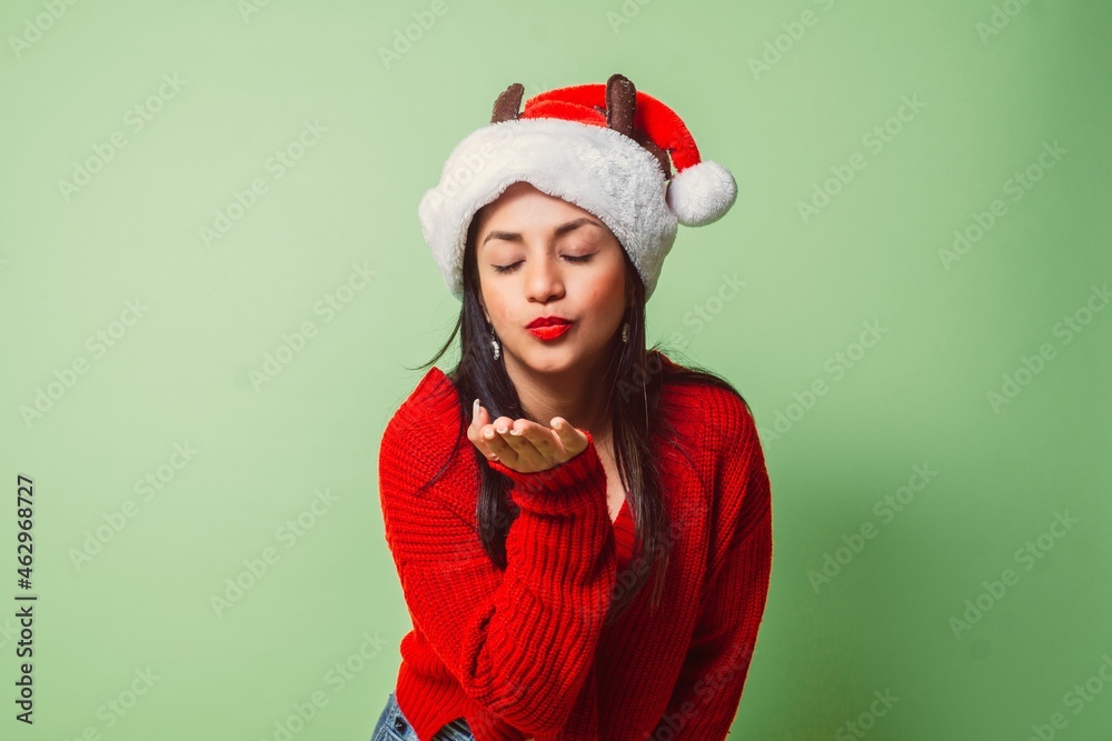 young woman with closed eyes, santa claus hat, sweater and red lips blowing a kiss. young woman with closed eyes, santa claus hat, sweater and red lips blowing a kiss.