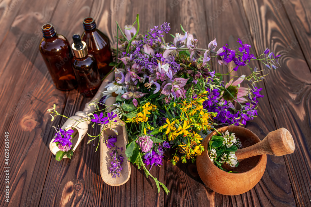 Obraz Summer medicinal herbs - St. John's wort, chamomile, clover near wooden mortar. Bottles for cosmetics from natural herbs fototapeta, plakat