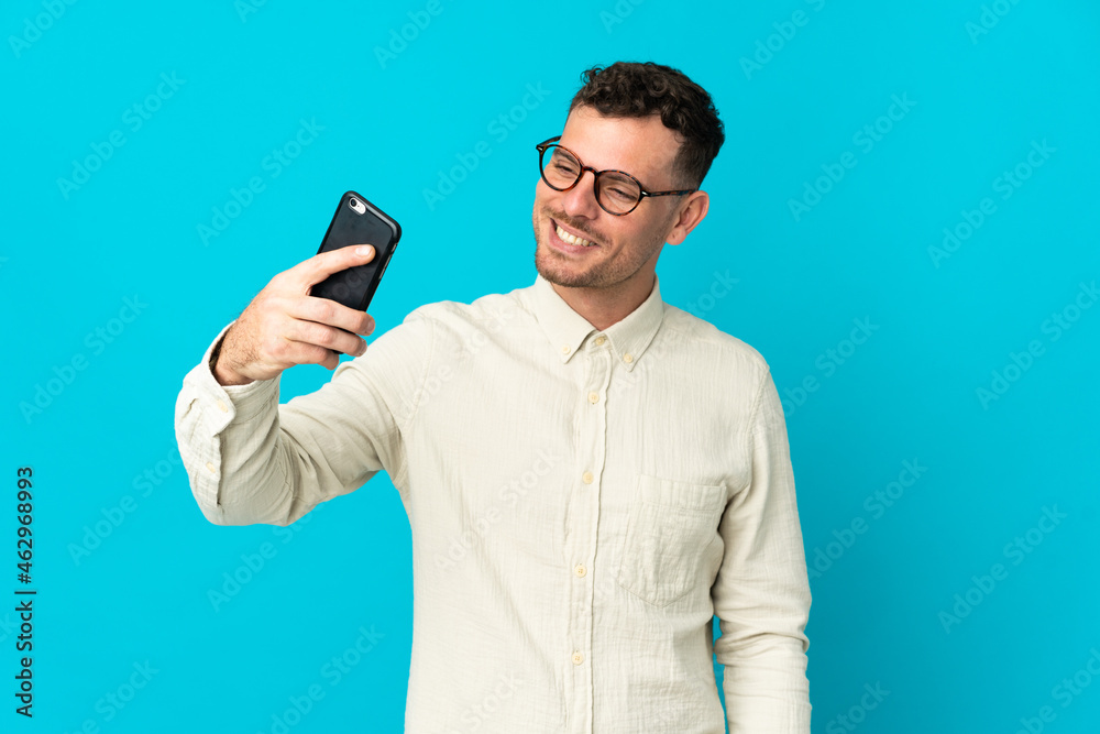 Young caucasian handsome man isolated on blue background making a selfie Young caucasian handsome man isolated on blue background making a selfie