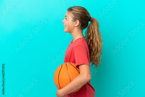 Little caucasian girl playing basketball isolated on blue background laughing in lateral position