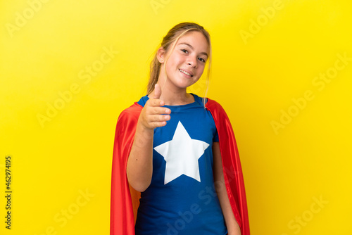 Super Hero little girl isolated on yellow background shaking hands for closing a good deal