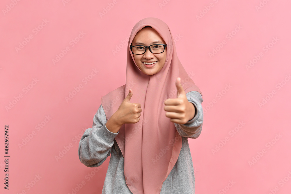 Young Asian Muslim woman showing thumbs up against pink colour background.
