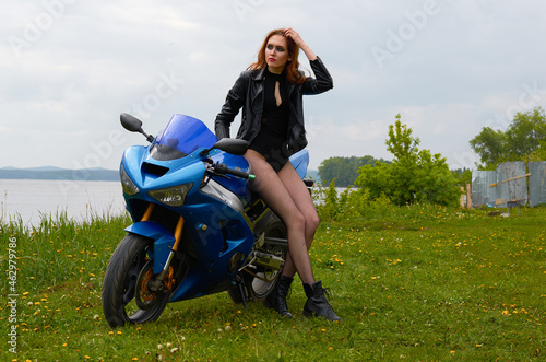 a young woman with red hair and wearing a black leather jacket on a blue sports motorcycle