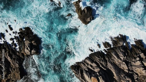 Island coastline with powerful waves breaks on the rocks, early in the morning. Aerial view over the mediterane ocean water at the steep cliffs. Drone circling upwards, Italy
