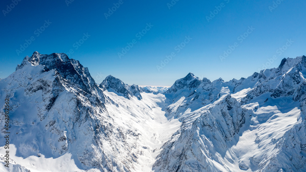 Caucasus Mountains, Panoramic view of the ski slope with the mountains Belalakaya, Sofrudzhu and Sulakhat on the horizon in winter day. Dombai ski resort, Western Caucasus, Karachai-Cherkess, Russia.