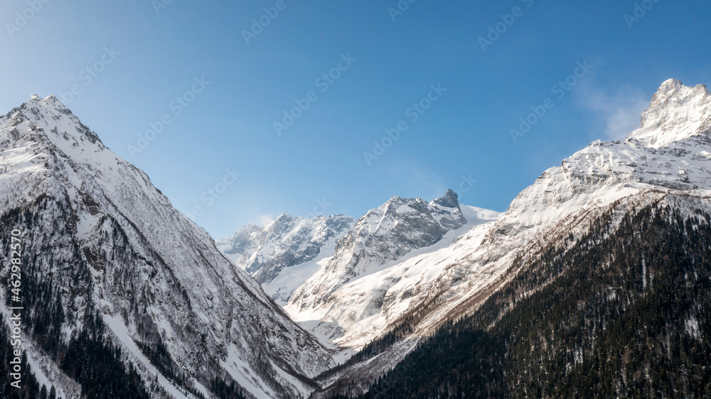Caucasus Mountains, Panoramic view of the ski slope with the mountains Belalakaya, Sofrudzhu and Sulakhat on the horizon in winter day. Dombai ski resort, Western Caucasus, Karachai-Cherkess, Russia.