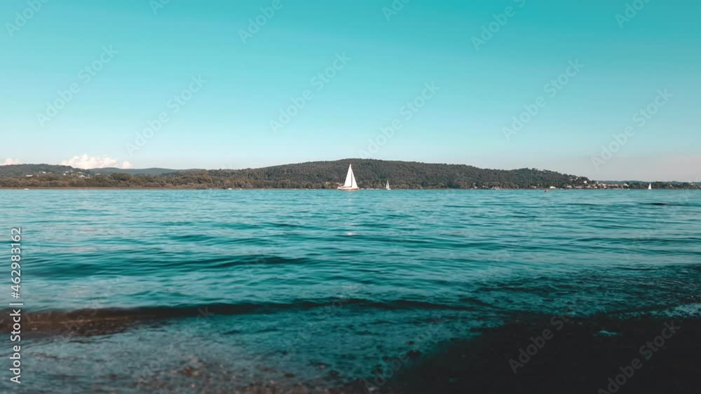 Cinematic teal colored low-angle view of yacht cruise in calm open lake waters of Maggiore lake in Italy Cinematic teal colored low-angle view of yacht cruise in calm open lake waters of Maggiore lake in Italy