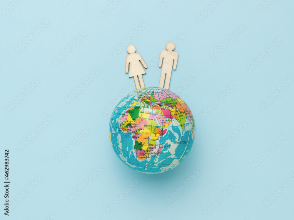 Male and female wooden figurines on a model of the globe on a blue background. Male and female wooden figurines on a model of the globe on a blue background.