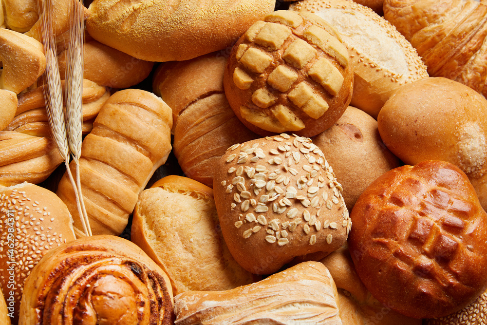 Close up of different types of breads and golden buns with ears of wheat. Food and bakery concept. Salty and sweet food. Bakery and carbohydrates.