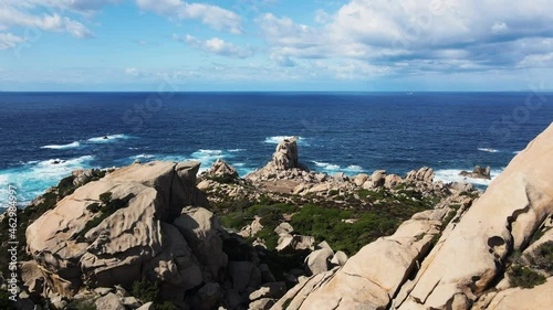 Aerial view forward, flying trouth two big rocks on the coastline, behind a noher big rock, the waves break into the bay. shaped by the water of the mediterranean sea and the wind. photo