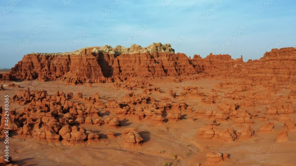 Gorgeous trucking left aerial drone shot of the beautiful Goblin Valley Utah State Park with small strange mushroom rock formations below and large red and white Butte's in the background.