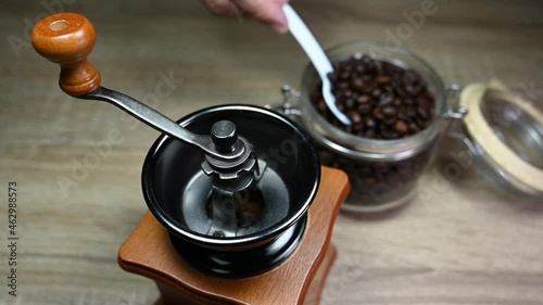 Left hand taking a spoon and then taking beans from the jar into the grinder; Coffee Grinder, Jar with Coffee Beans, Spoon. photo