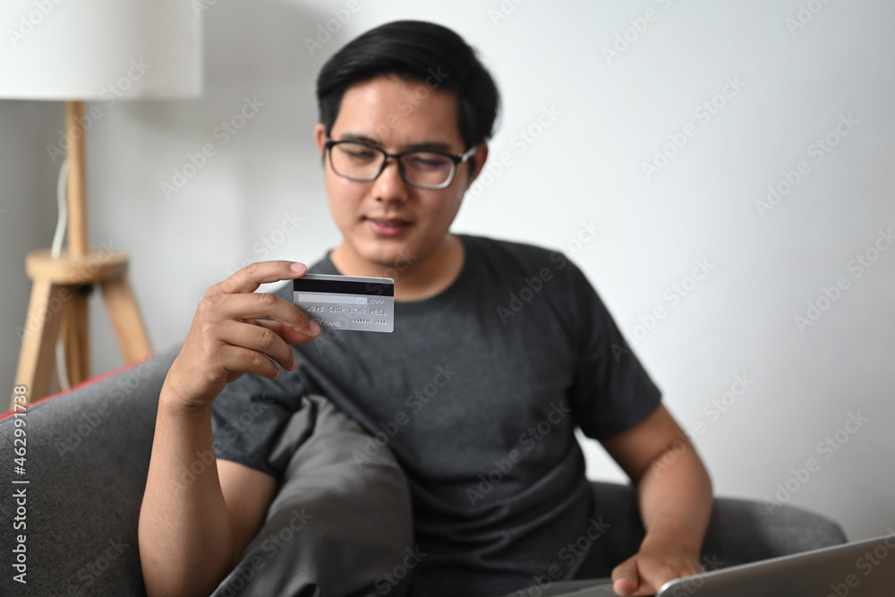 Young asian man using laptop computer and holding credit card. Young asian man using laptop computer and holding credit card.