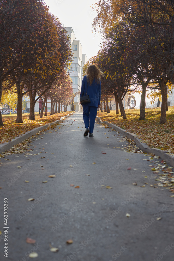 a young girl in an electric blue pantsuit walks alone after work in an autumn park in the afternoon in sunny weather