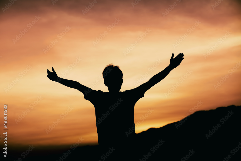Man pray with arms stretched out to a sunset sky, christian silhouette concept.