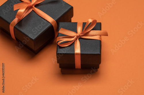 Black gift boxes tied with orange ribbons on an orange background. Halloween concept.