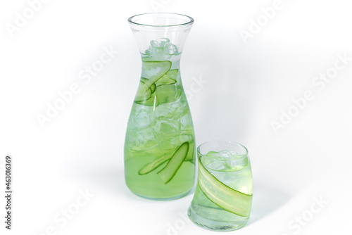 Clear fresh cool cucumber lemonade in a glass and pitcher with ice and cucumber slices isolated on a white background