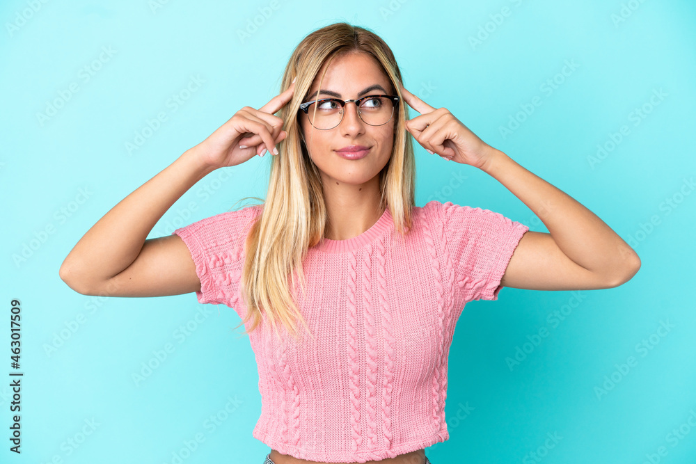 Blonde Uruguayan girl isolated on blue background having doubts and thinking Blonde Uruguayan girl isolated on blue background having doubts and thinking