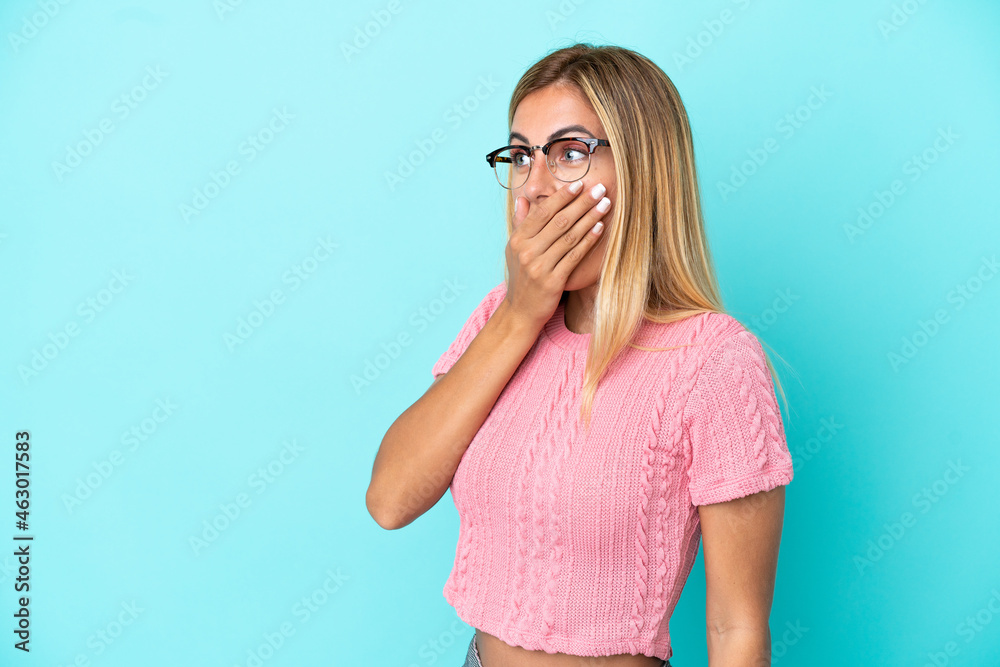 Blonde Uruguayan girl isolated on blue background doing surprise gesture while looking to the side Blonde Uruguayan girl isolated on blue background doing surprise gesture while looking to the side