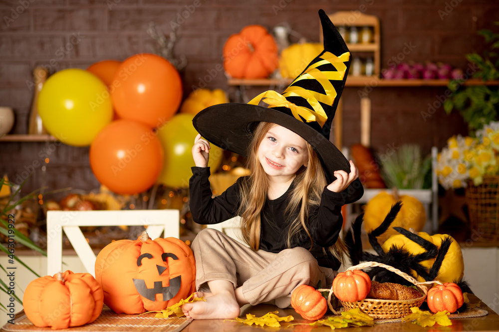 halloween, a cute smiling child girl in a witch costume in a dark kitchen with pumpkins and a big spider and festive decor during the Halloween celebration rejoices halloween, a cute smiling child girl in a witch costume in a dark kitchen with pumpkins and a big spider and festive decor during the Halloween celebration rejoices