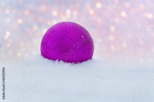 A pink New Year ball lies on the sparkling snow outdoors on a frosty winter day. Christmas toys. Space for text. Christmas  festive design.The concept of Christmas and New Year.Bokeh in the background