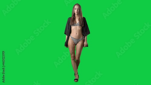 Sexy slim young woman fashion model in bikini and beach tunic walking to camera. Full body on green screen chroma key background
