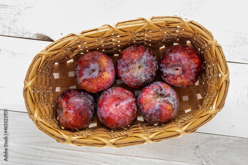 Several juicy organic, purple plums in a basket, close-up, top view.