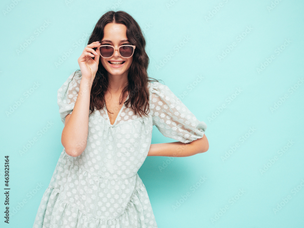 Closeup portrait of young beautiful smiling female in trendy summer dress.Sexy carefree woman posing near blue wall in studio.Positive model having fun indoors.Cheerful and happy. Takes off sunglasses Closeup portrait of young beautiful smiling female in trendy summer dress.Sexy carefree woman posing near blue wall in studio.Positive model having fun indoors.Cheerful and happy. Takes off sunglasses