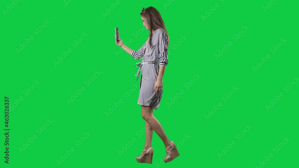 Side view of walking woman in beach wear taking selfie photos with cell phone. Full body on green screen chroma key background Side view of walking woman in beach wear taking selfie photos with cell phone. Full body on green screen chroma key background