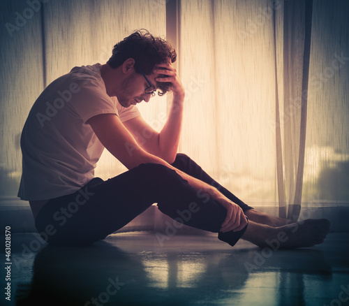 Принти на полотні Hopeless caucasian man sitting alone by the window in silhouette with sadness on the floor